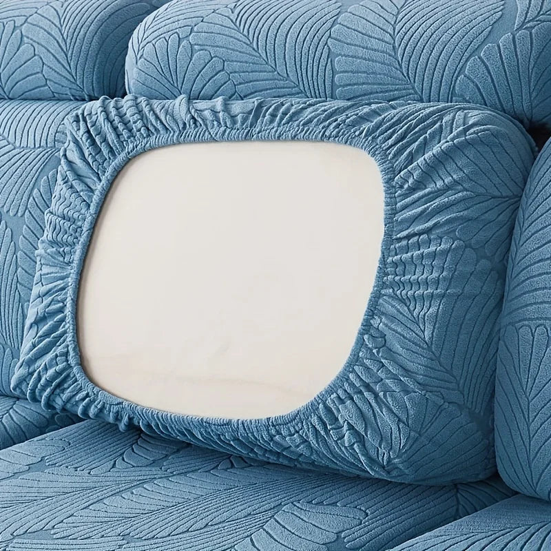 A close-up of a blue leaf pattern sofa slipcover featuring a square cutout revealing a light cream cushion.