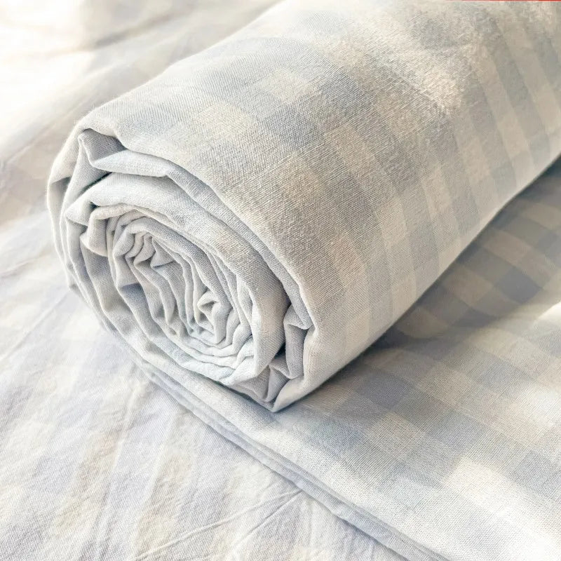 A rolled light gray plaid organic cotton bedding set on a sheet.