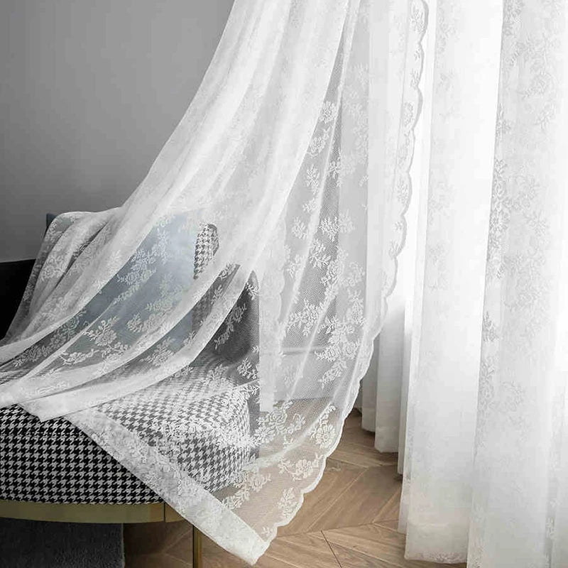 White sheer floral lace window curtains draped over a table.