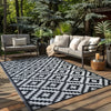A black and white geometric outdoor rug placed on a wooden deck surrounded by greenery.