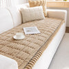 A beige quilted flannel sofa pad cover placed on a white sofa with cream pillows.