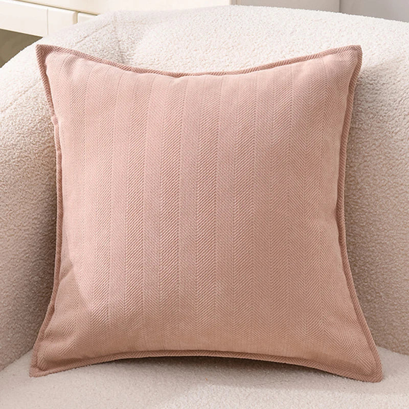 A square, light pink chenille throw pillow cover with vertical ribbing resting on a beige sofa.