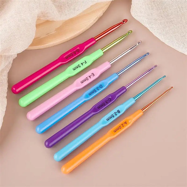 A collection of various colored precision aluminum alloy knitting and crochet hooks laid out on a light background.