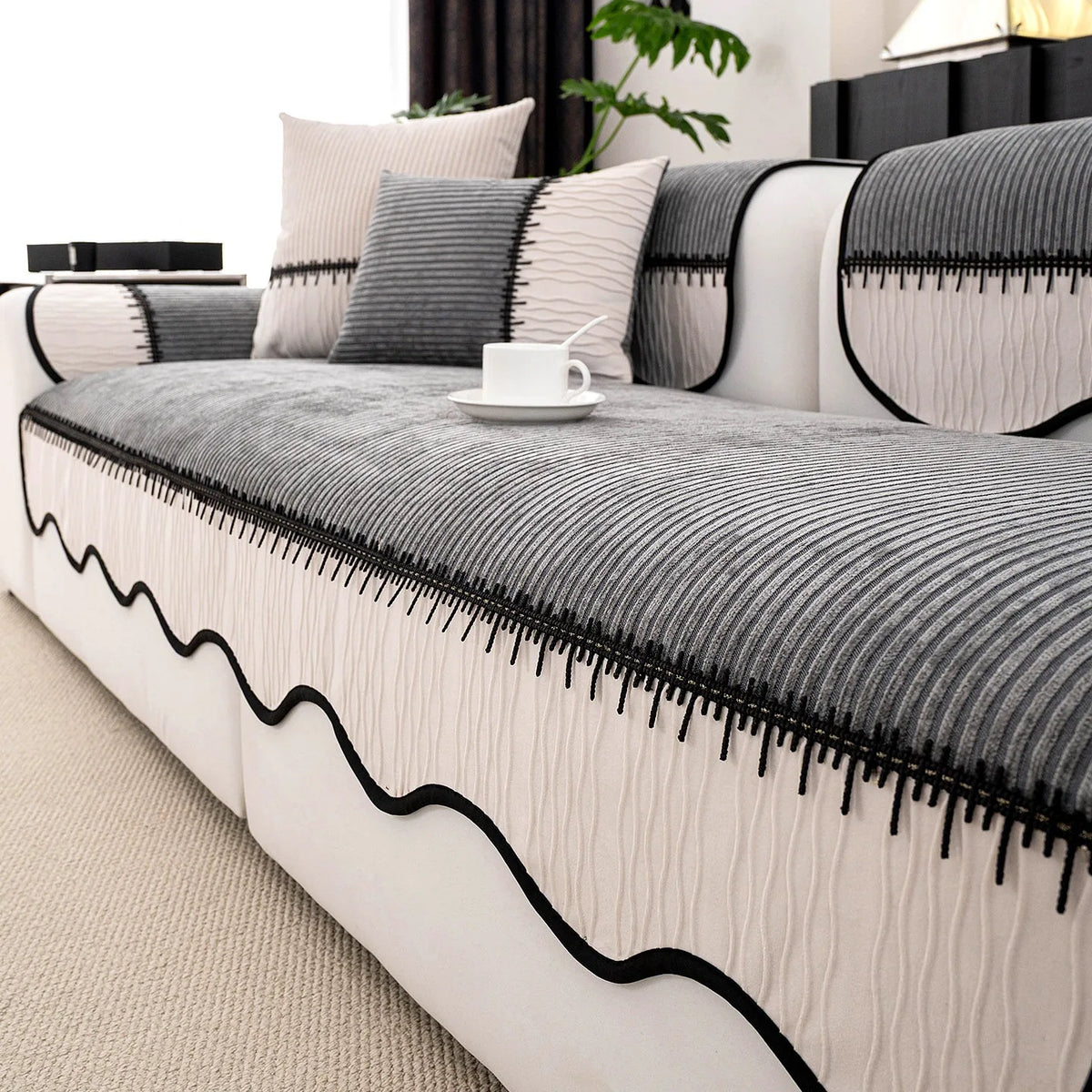 A close-up of a striped chenille pleated sofa cover in gray and white with black trim.