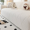 A cream-colored stretch sofa cover featuring vertical pleats and decorative accent pillows.