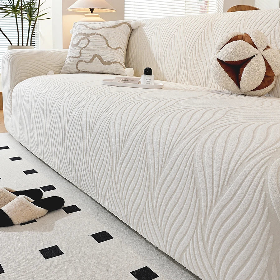 A cream-colored stretch sofa cover featuring vertical pleats and decorative accent pillows.