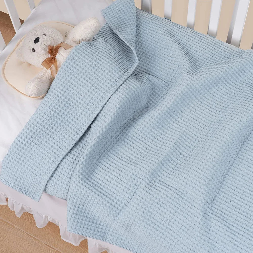 Light blue waffle blanket draped over a white crib mattress with a stuffed animal.
