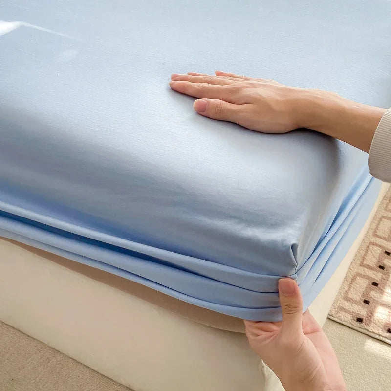 A hand is gently touching a light blue fitted bed sheet on a mattress.