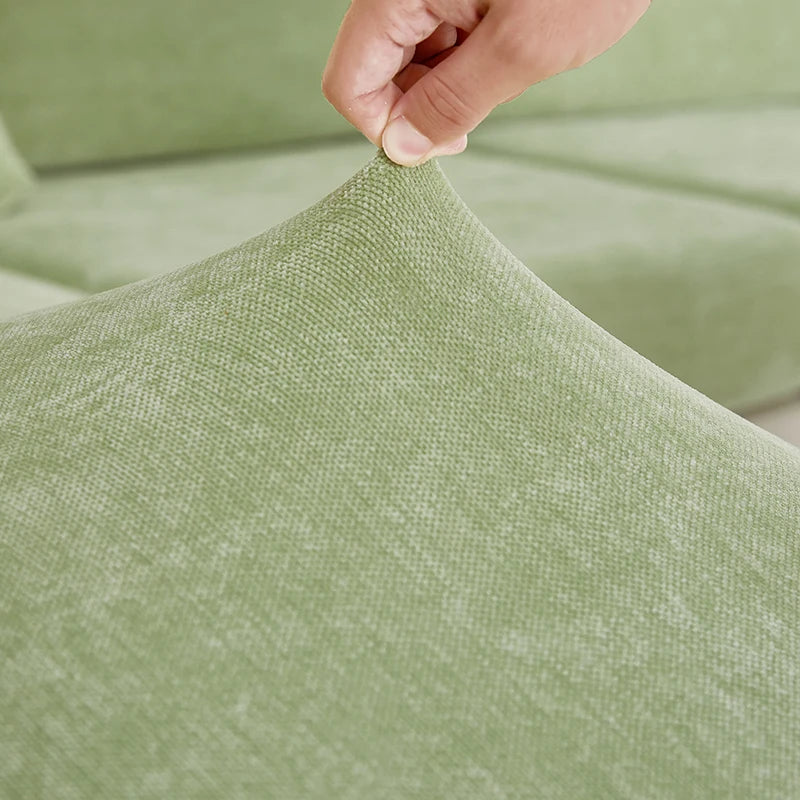 A hand is adjusting the fabric of a sage green stretchable chenille sofa cushion cover.