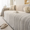 A beige and black fishbone pattern sofa cover with a cream pillow and a white cup on a light-colored bed.