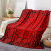 A vibrant red throw blanket featuring a black symmetrical spider web pattern draped over a light-colored sofa.