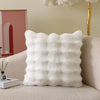 A white fluffy cushion cover with vertical pleats resting on a beige sofa.