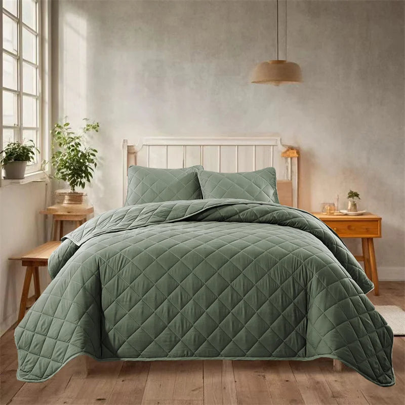 A teal quilted bedspread set is displayed on a bed in a bright, minimalist bedroom with light wood flooring and white walls.