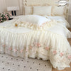 A white Korean style lace embroidered duvet set with pink floral embroidery and ruffled edges on a bed.