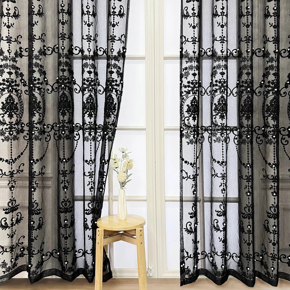 Black sheer curtain featuring intricate pearl and lace embroidery hanging in a window frame.