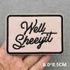 Pink embroidered patch with the text Well Sheeijit on a gray fabric background