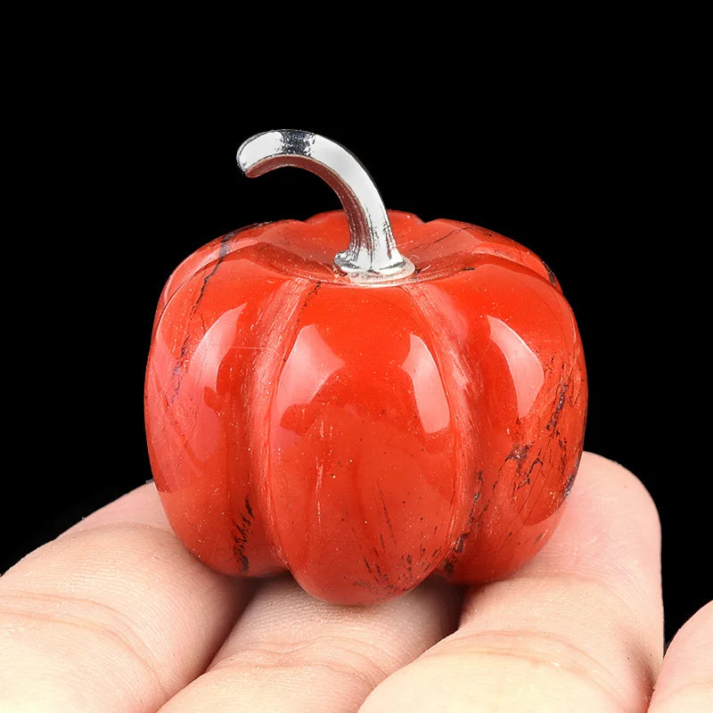 A handcrafted natural stone pumpkin figurine with a silver stem resting in a person's hand.