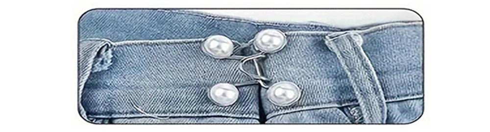 A close-up of a denim jean waistband with an adjustable alloy button clip featuring several pearl-like buttons.