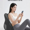 A woman is sitting on an ergonomic memory foam pillow while using a smartphone.