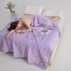 A purple breathable cooling blanket is draped over a person lying down on a white surface.