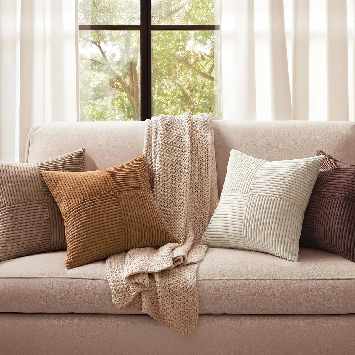 A set of four neutral corduroy throw pillow covers with a patchwork design displayed on a light-colored sofa.