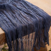 A dark blue crinkled cheesecloth table runner draped on a wooden table.