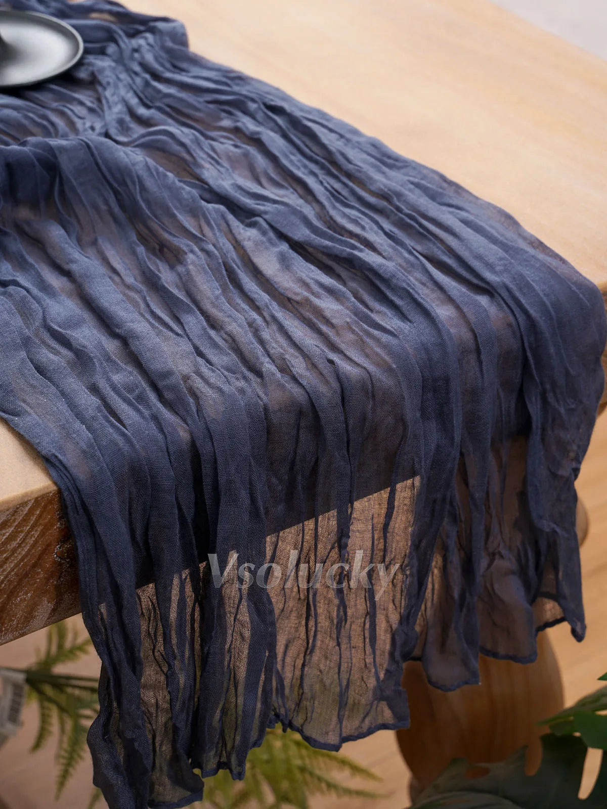 A dark blue crinkled cheesecloth table runner draped on a wooden table.