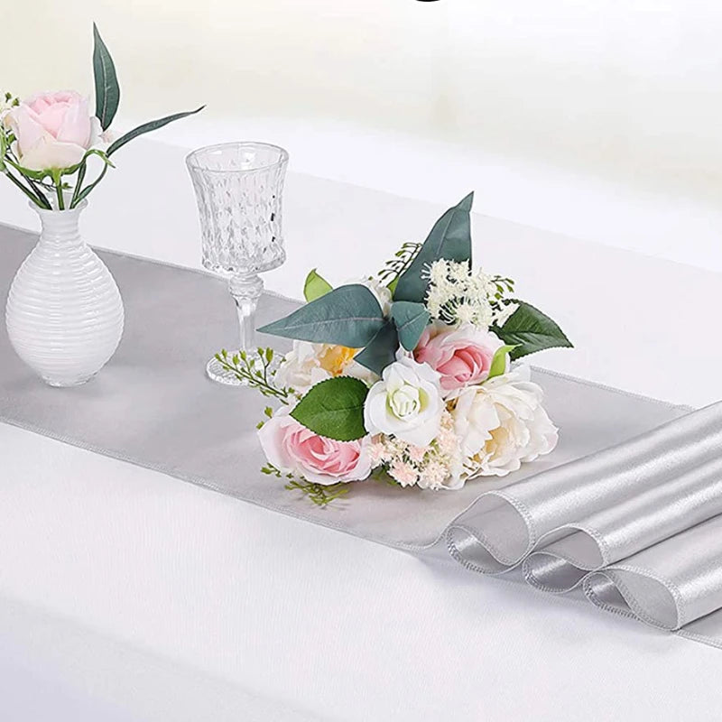 Luxury satin table runner with pink and white floral arrangements and silver glassware.