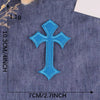 A single bright blue cross embroidery patch on a dark denim fabric background.