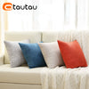 A collection of colorful linen cushion covers in shades of blue, gray, white, and orange displayed on a light sofa.