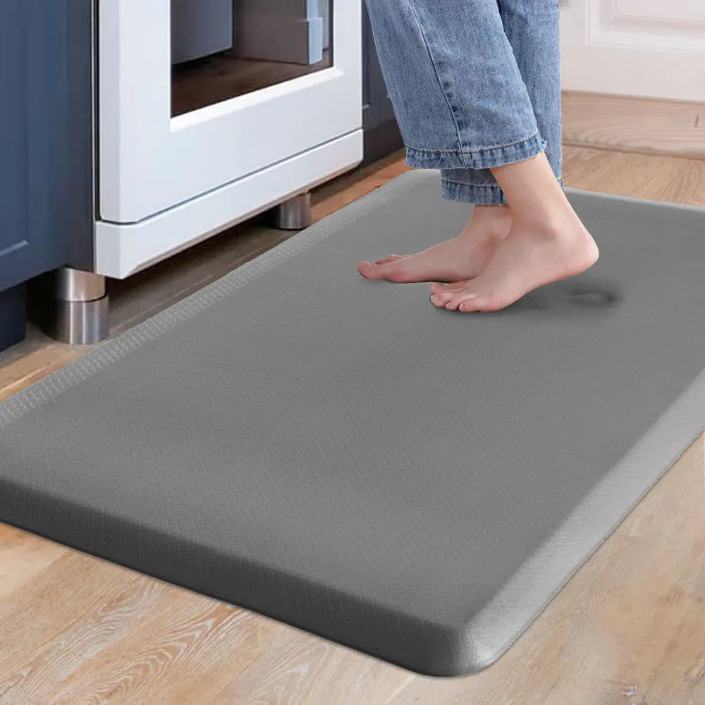 A gray anti-fatigue PVC kitchen mat placed on a light wood floor next to a white appliance.