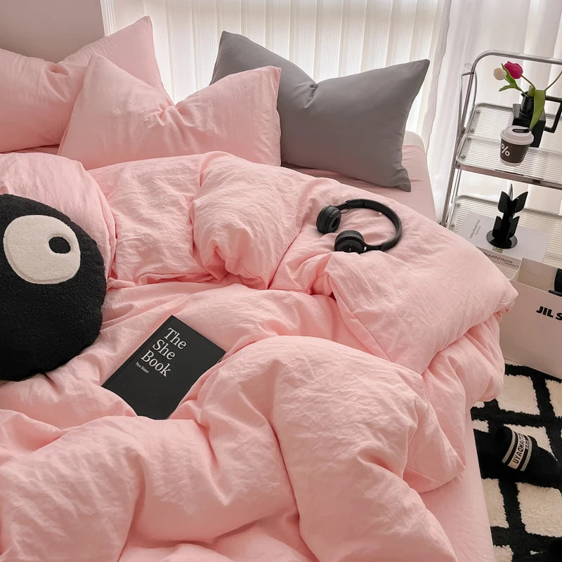 A pink duvet cover set with matching pillows and a gray pillow, displayed on a bed.