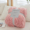 A pink plush throw blanket with a quilted texture is displayed on a white surface.