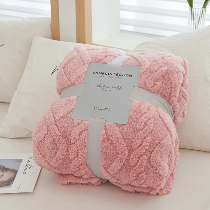 A pink plush throw blanket with a quilted texture is displayed on a white surface.