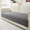 A gray geometric quilted sofa cushion cover placed on a cream-colored sofa.