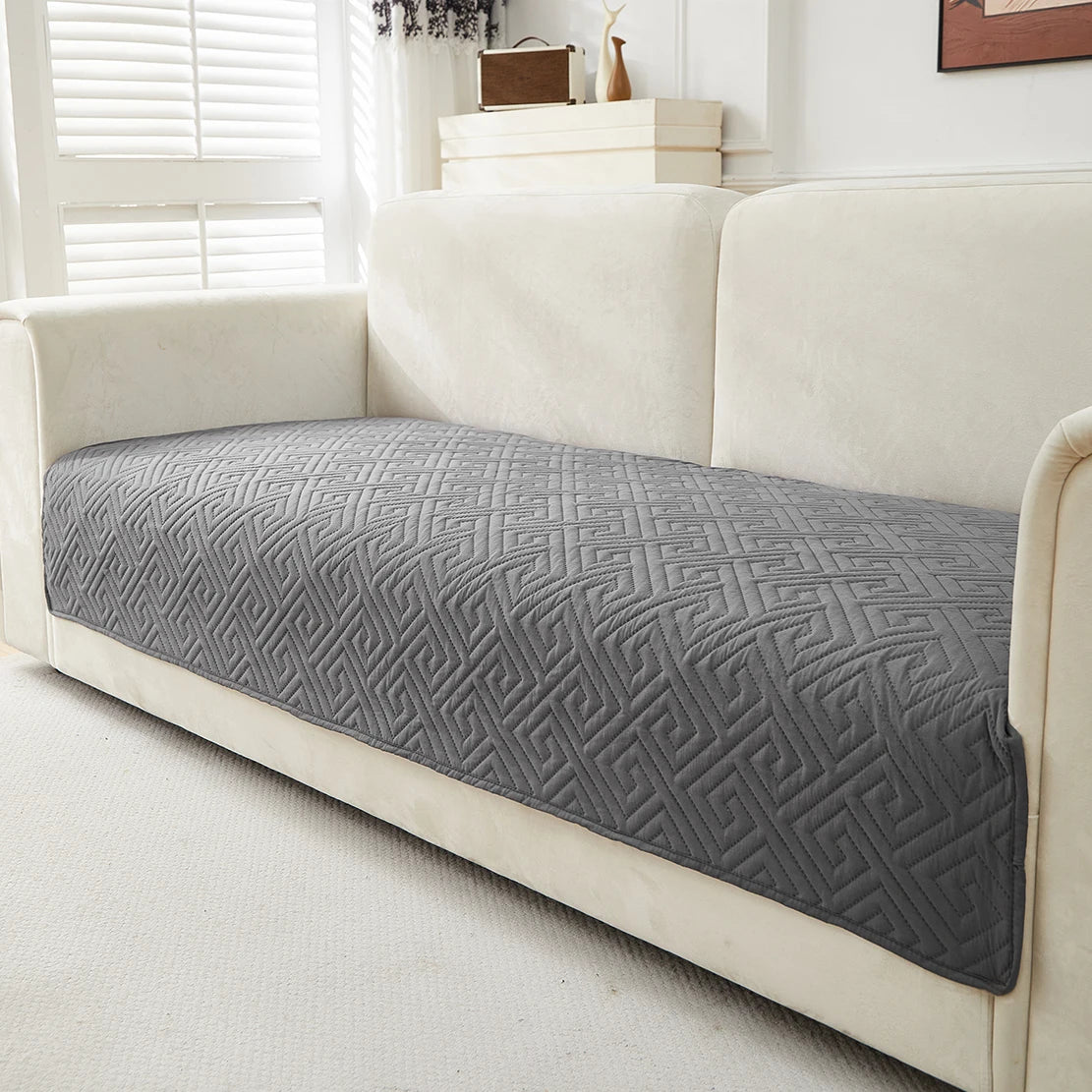 A gray geometric quilted sofa cushion cover placed on a cream-colored sofa.