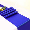 A stack of royal blue satin fabric rolls laid on a white surface with a small yellow floral accent.