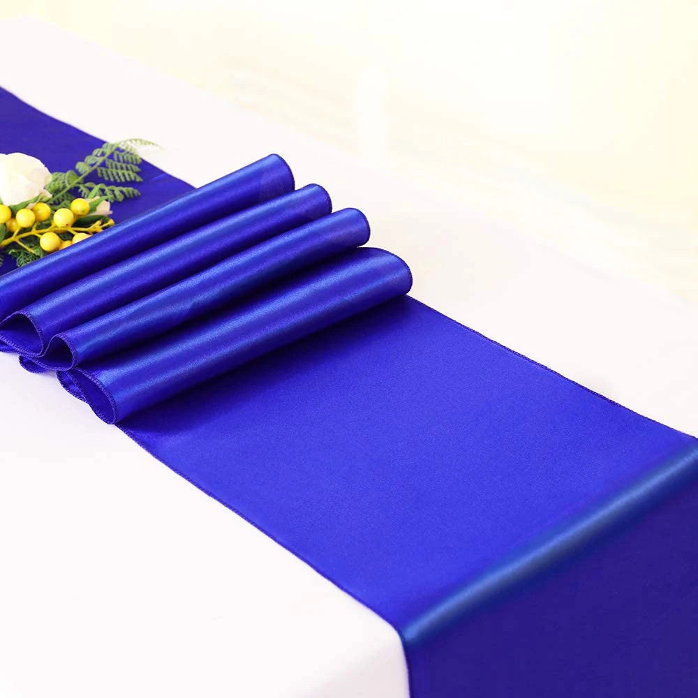 A stack of royal blue satin fabric rolls laid on a white surface with a small yellow floral accent.