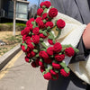 A close-up of a handmade floral bouquet knitted from red and green yarn, held in a white woven throw blanket.