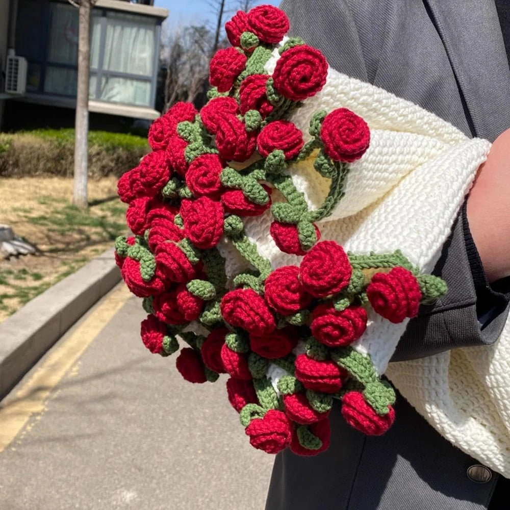 A close-up of a handmade floral bouquet knitted from red and green yarn, held in a white woven throw blanket.