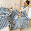 A person is wrapped in a fluffy light blue fleece throw blanket indoors next to a lamp.