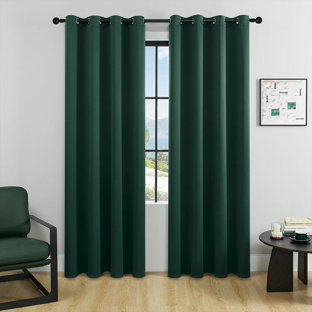 A pair of dark green blackout window curtains hanging on a rod in a bright room.