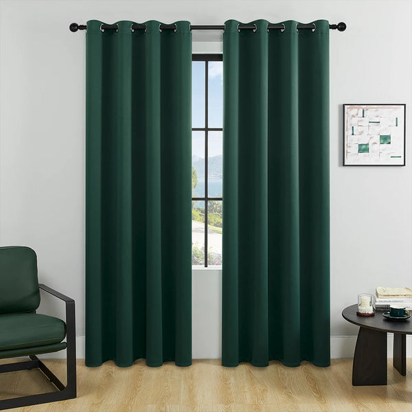 A pair of dark green blackout window curtains hanging on a rod in a bright room.
