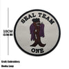 A round gray embroidered patch for a Seal Team member featuring a stylized dark brown figure and the text ONE.