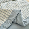 A close-up of a light blue and white striped luxury jacquard summer quilt folded on a bed.
