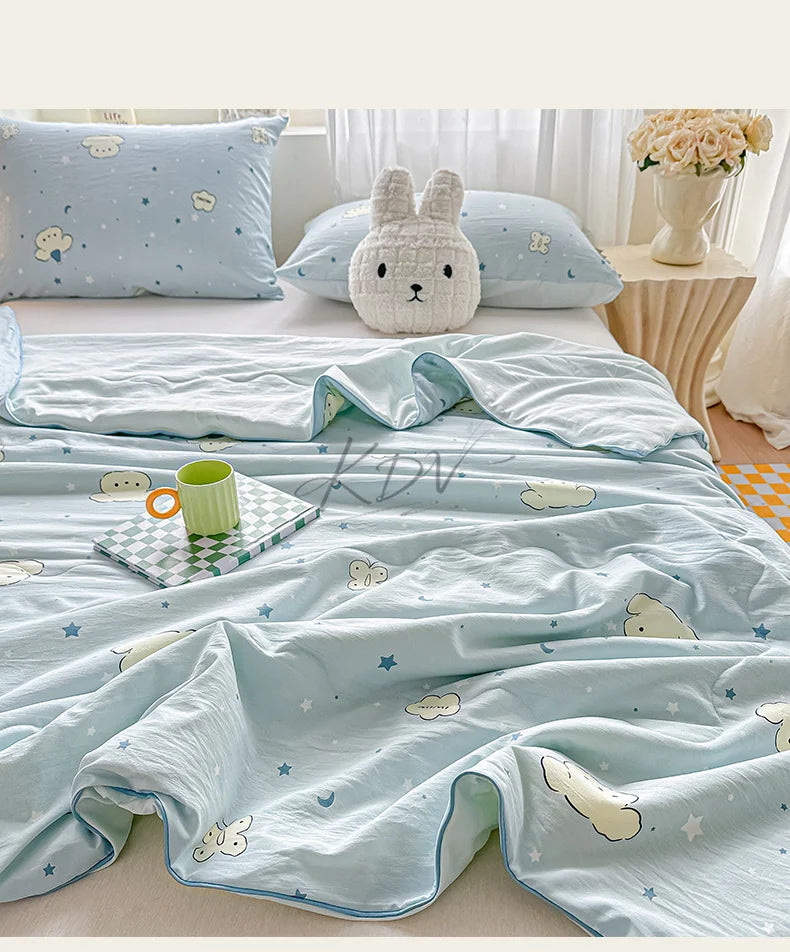 Light blue quilt blanket with a pastoral print featuring clouds, stars, and sheep on a bed.