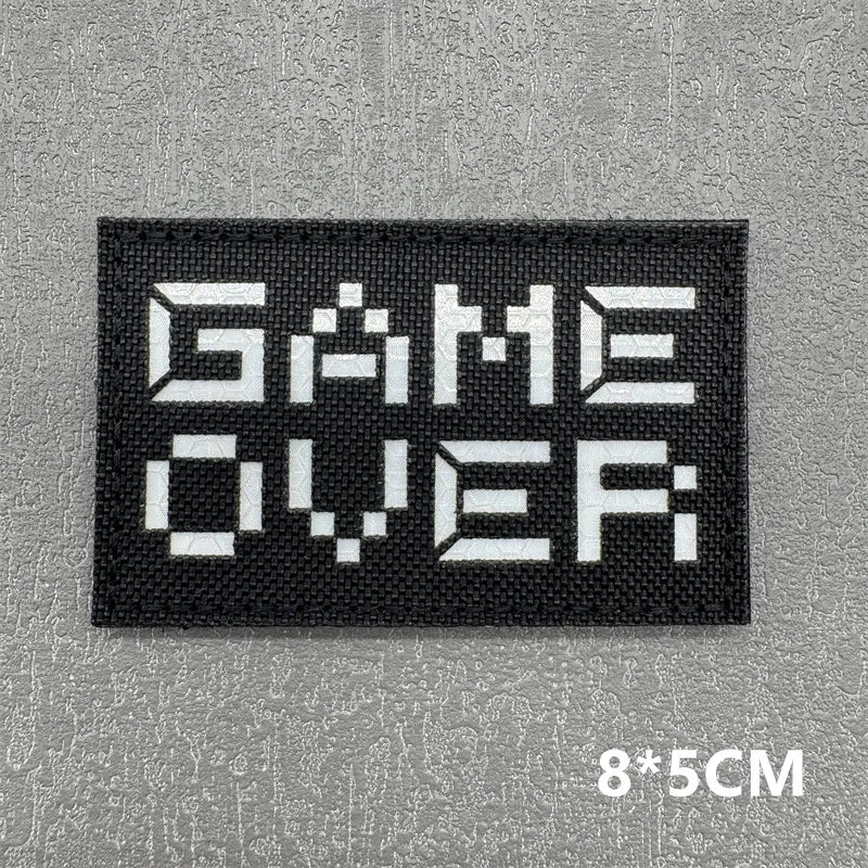 Black embroidered patch with white text GAME OVER on a gray textured background