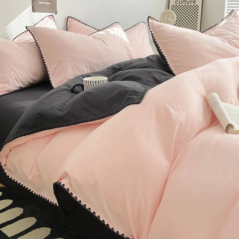 A close-up of a pink and gray bed linen set featuring pillows and a duvet on a dark bed.