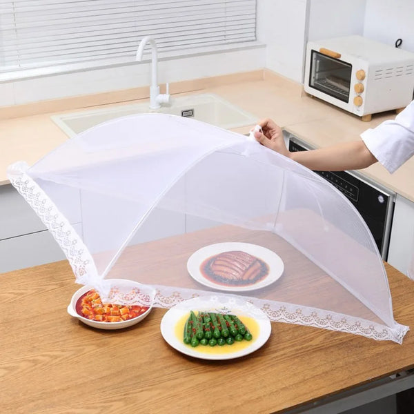 A white foldable mesh insect and fly protection cover is placed over a plate of cooked meat and a plate of green vegetables o