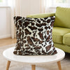 A close-up of a brown and white leopard print throw pillow resting on a white round table.